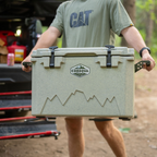 Close-up of a man holding a tan hard cooler by both handles in front of a truck bed