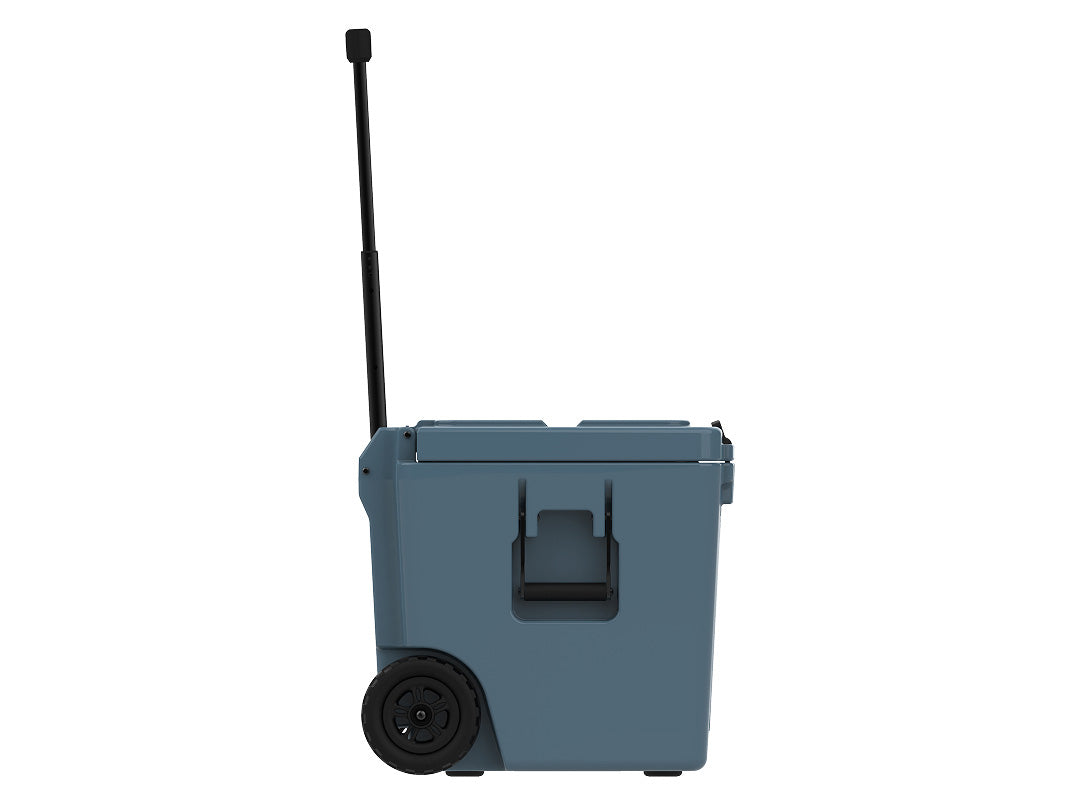 Side view of the slate-blue wheeled cooler with the handle raised, a molded grab handle and a wheel