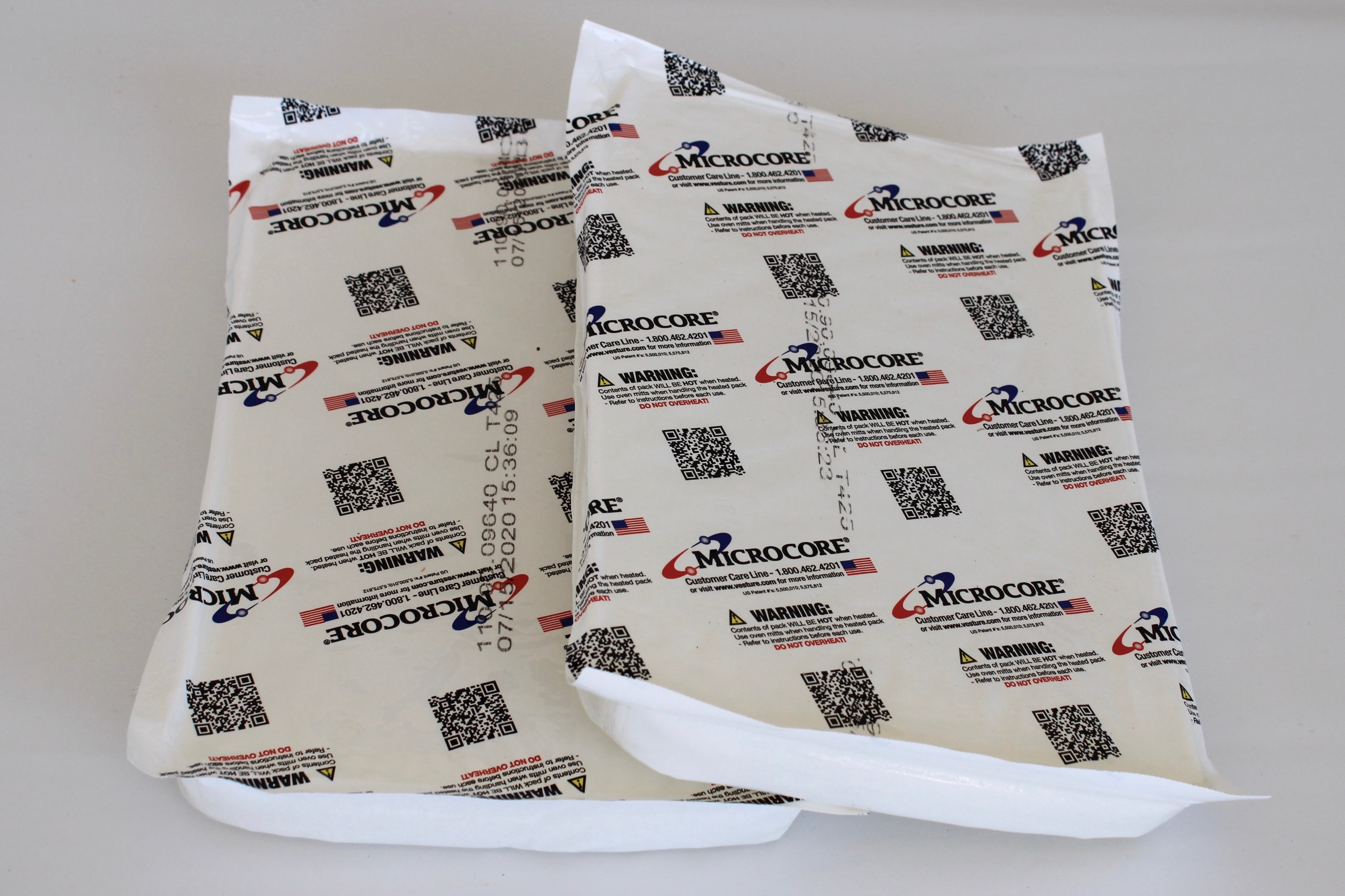 Two flat white heat packs printed with Microcore logos, QR codes and warning labels, on white