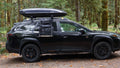 Load image into Gallery viewer, Black SUV in a forest with the kitchen bag hanging open from its roof rack beside the rear door
