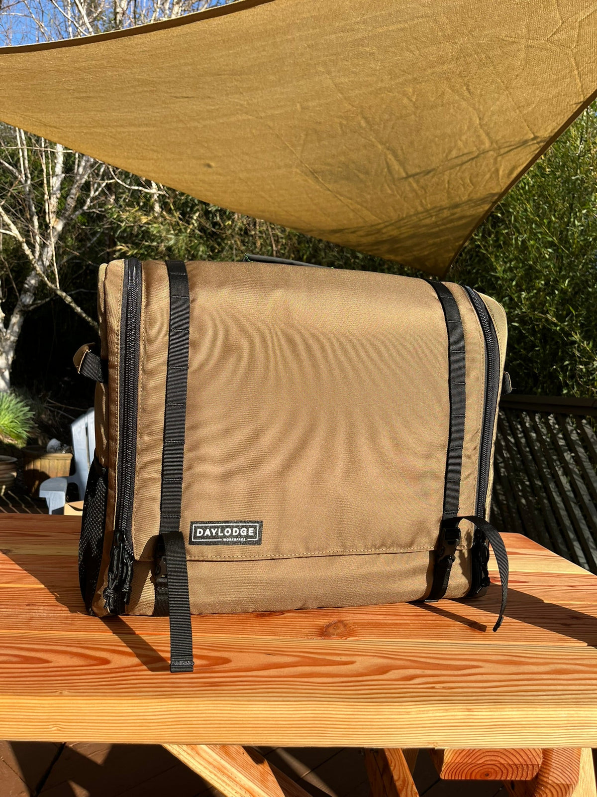 Closed brown kitchen bag on a wooden picnic table under a tan shade sail