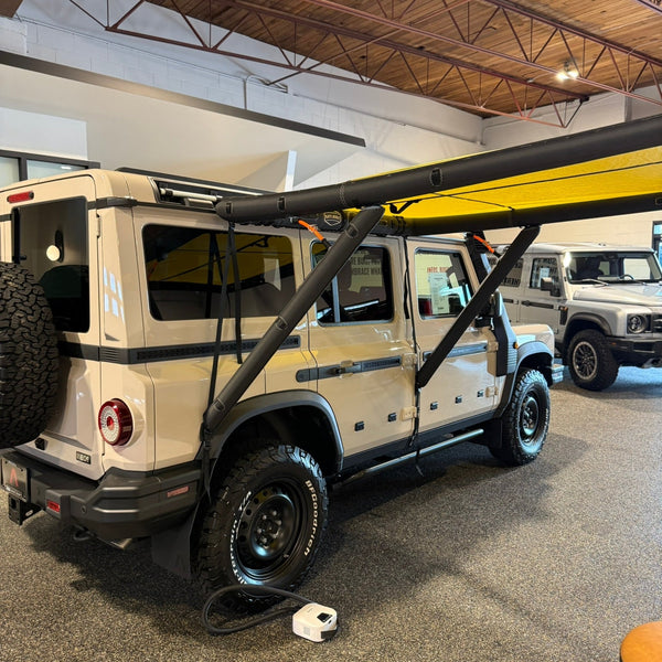 Inflatable yellow awning extended from the side of a tan SUV in a showroom, a small pump on the floor