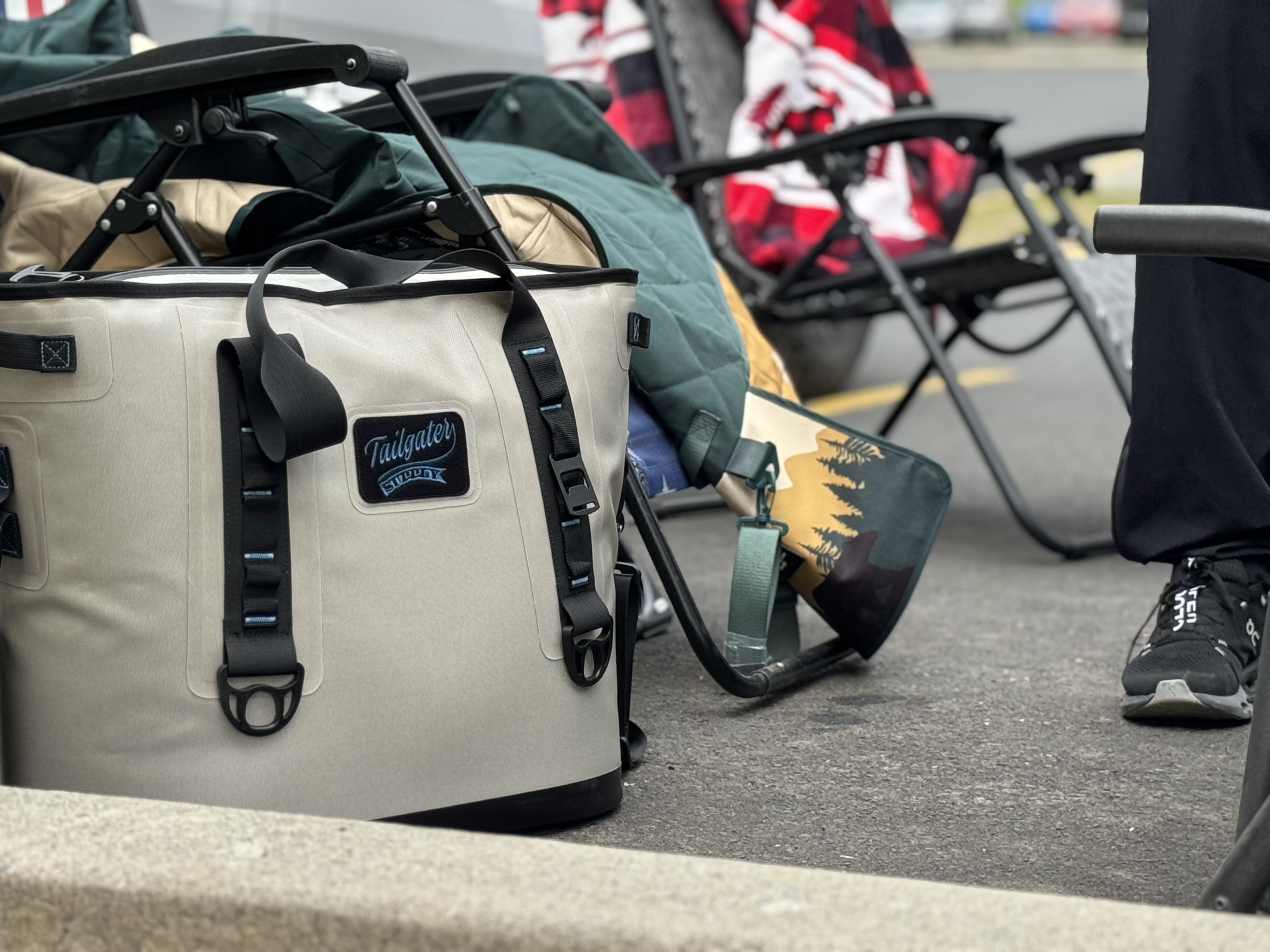 Sidekick tote cooler on the curb at a tailgate next to folding chairs and blankets