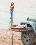 Load image into Gallery viewer, Tire Table on a Jeep's tire at the beach, holding a camp stove and a glass of wine.
