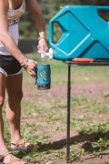 Load image into Gallery viewer, Woman filling a mug from a water jug set on a Tire Table outdoors.
