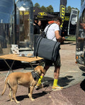 Load image into Gallery viewer, Man carrying a gray kitchen bag on his shoulder at an outdoor expo, a dog at his feet
