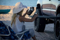 Load image into Gallery viewer, Woman in a sun hat pouring a drink at a Tire Table on an SUV's tire by the water.
