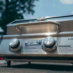 Low-angle view of the closed grill's lid handle and two control knobs outdoors