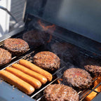 Burgers and hot dogs cooking over flame on the grates of the open grill