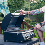 Man lifting the lid of a tabletop grill on a deck table to flip a burger