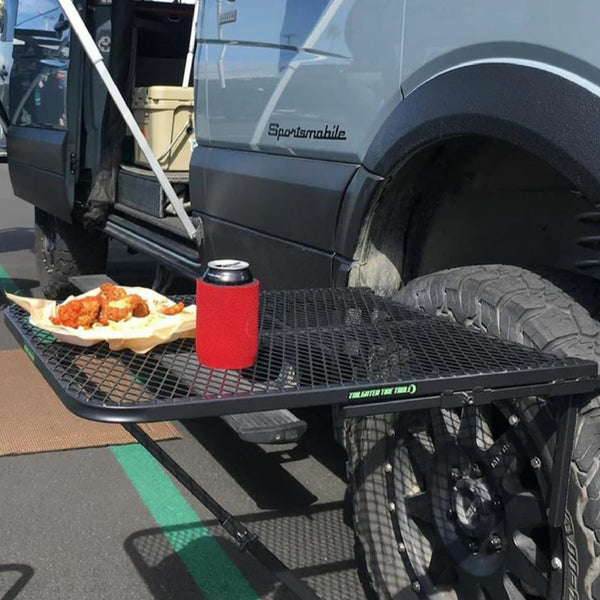 Large steel tire table mounted on a van's rear tire, holding wings and a can in a koozie at a tailgate