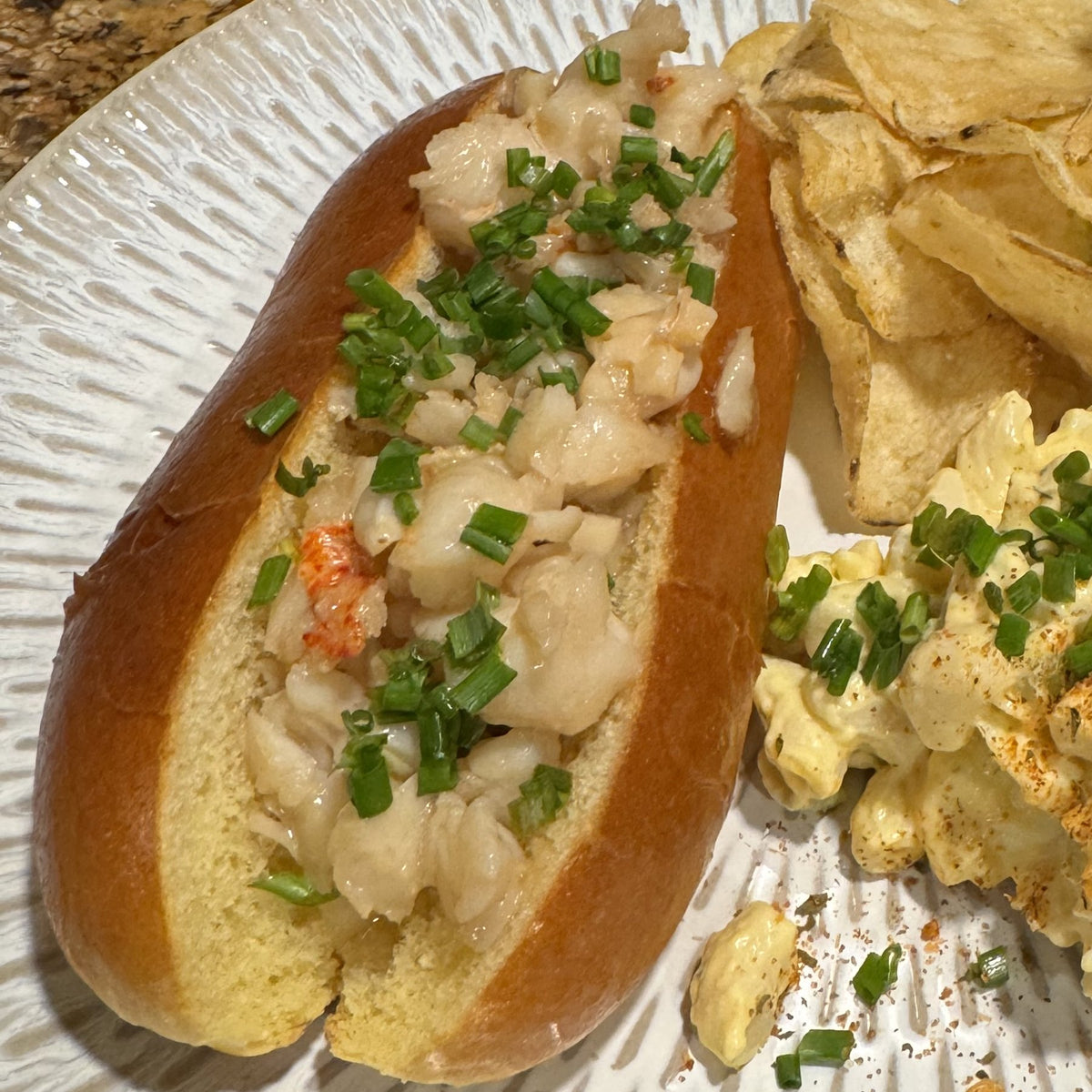 A Connecticut lobster roll: warm buttered lobster and chives in a toasted bun, with chips and macaroni salad