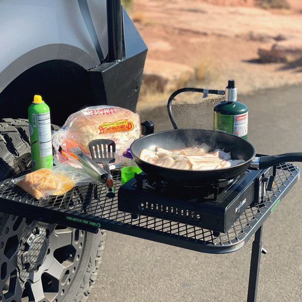 Tire Table on an SUV's front tire with a camp stove frying breakfast, buns and condiments on the table