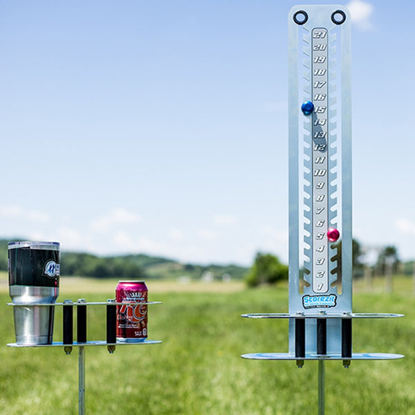 Scorezit score tower and Drinkit holder on ground stakes in a field, holding a tumbler and a soda can