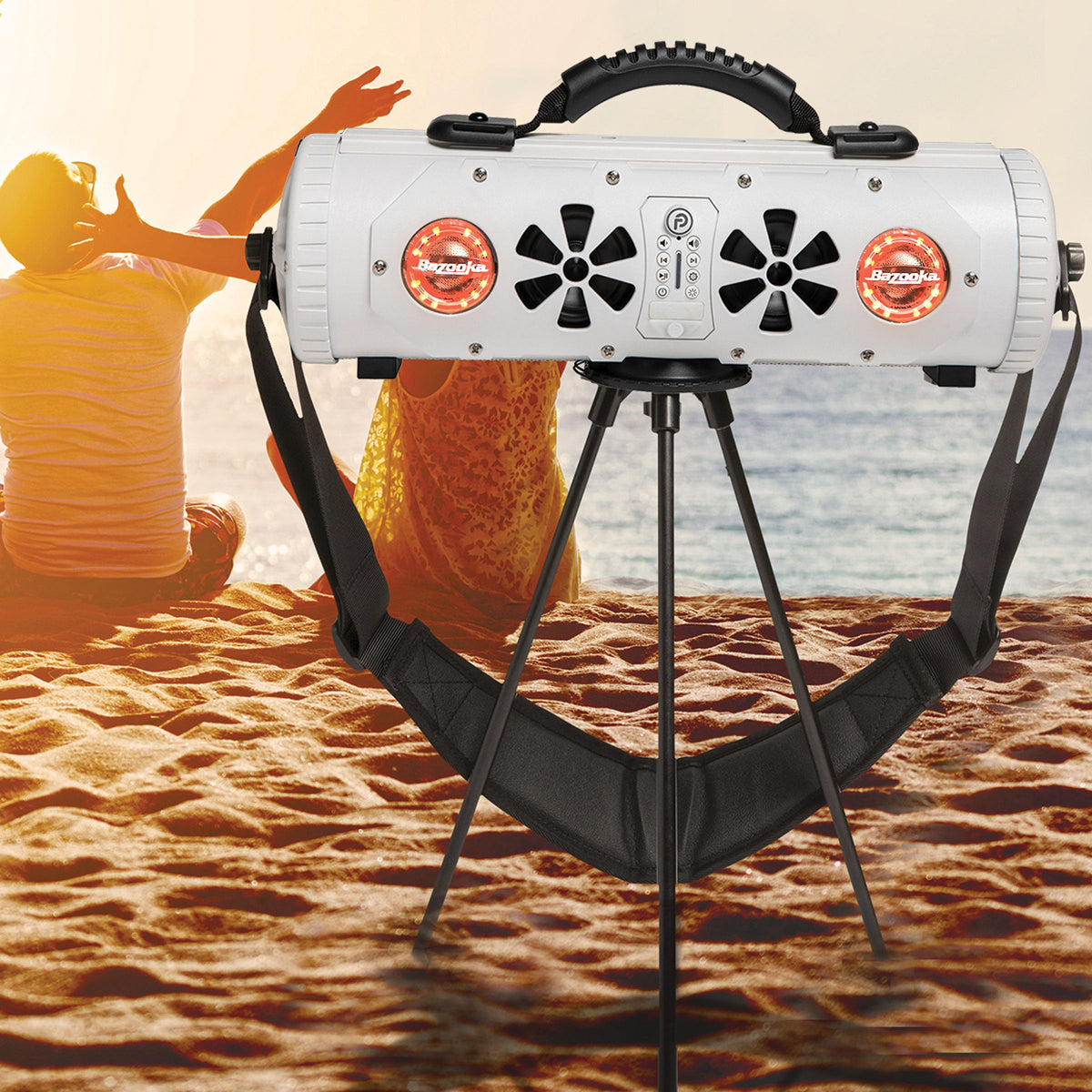 White Party Bar MINI on its tripod on a beach at sunset, with two people sitting on the sand behind it
